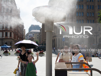 People are trying to reach the mist sprinkler during the heatwave at the Bund in Shanghai, China, on July 3, 2024. (