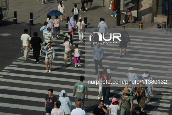 People are walking across the street during the heatwave on Nanjing Road in Shanghai, China, on July 3, 2024. 