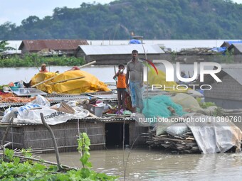 Villagers are taking shelter on the top of their partially submerged hut in a flood-affected area in Morigaon District of Assam, India, on J...