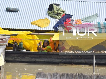 A woman is taking shelter on a boat as her house is submerging during floods in Morigaon district in Assam, India, on July 3, 2024. (