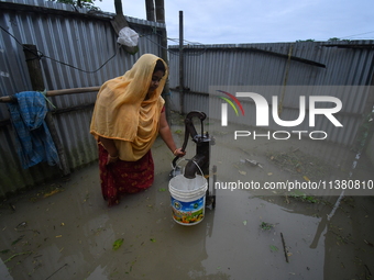 A woman is fetching water from a partially submerged hand pump in a flood-affected village in Nagaon district of Assam, India, on July 2, 20...