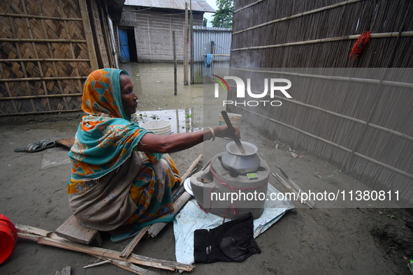 A woman is cooking inside her partially submerged house in the Bhurbandha village in Nagaon district of Assam, India, on July 2, 2024. 