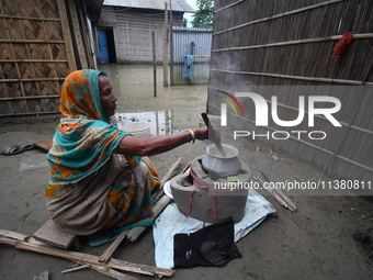 A woman is cooking inside her partially submerged house in the Bhurbandha village in Nagaon district of Assam, India, on July 2, 2024. (