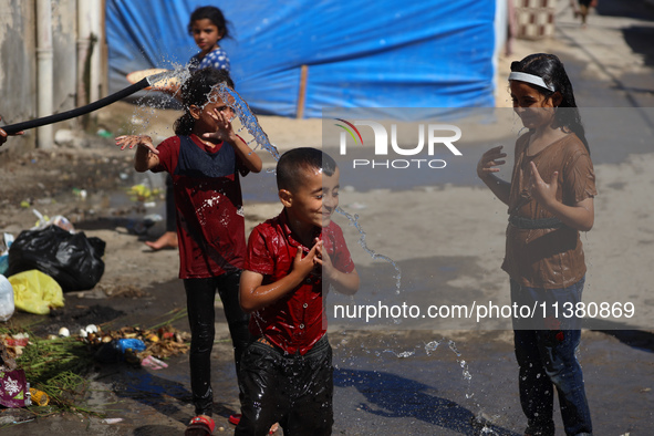 A displaced Palestinian boy is spraying children with water from a pipe outside their tents during a heat wave in Deir al-Balah in the centr...