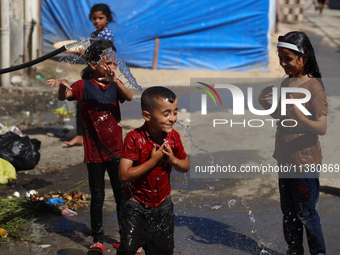 A displaced Palestinian boy is spraying children with water from a pipe outside their tents during a heat wave in Deir al-Balah in the centr...