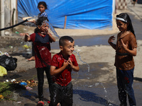 A displaced Palestinian boy is spraying children with water from a pipe outside their tents during a heat wave in Deir al-Balah in the centr...