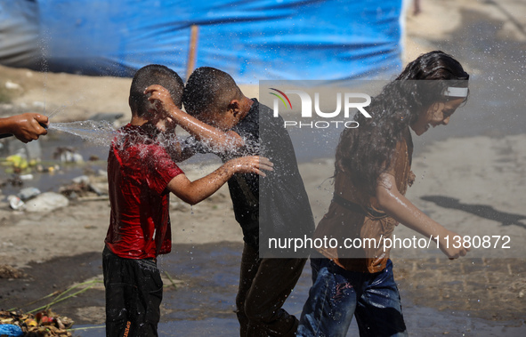 A displaced Palestinian boy is spraying children with water from a pipe outside their tents during a heat wave in Deir al-Balah in the centr...