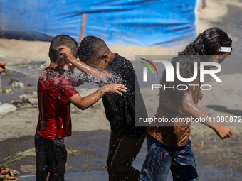 A displaced Palestinian boy is spraying children with water from a pipe outside their tents during a heat wave in Deir al-Balah in the centr...