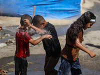 A displaced Palestinian boy is spraying children with water from a pipe outside their tents during a heat wave in Deir al-Balah in the centr...