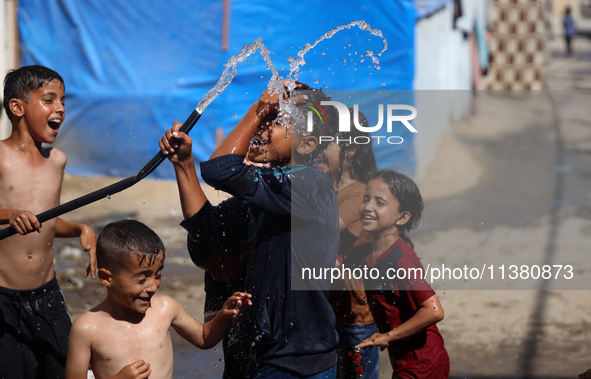 A displaced Palestinian boy is spraying children with water from a pipe outside their tents during a heat wave in Deir al-Balah in the centr...