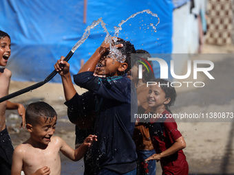 A displaced Palestinian boy is spraying children with water from a pipe outside their tents during a heat wave in Deir al-Balah in the centr...