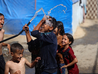 A displaced Palestinian boy is spraying children with water from a pipe outside their tents during a heat wave in Deir al-Balah in the centr...