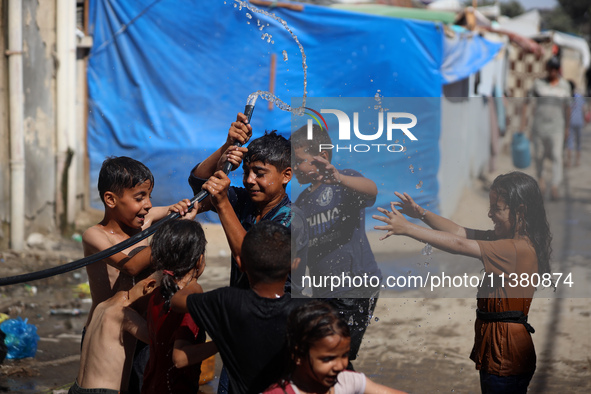 Displaced Palestinian children are playing with water outside their tents during a heat wave in Deir al-Balah in the central Gaza Strip on J...