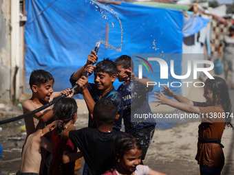 Displaced Palestinian children are playing with water outside their tents during a heat wave in Deir al-Balah in the central Gaza Strip on J...