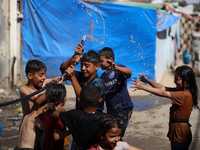 Displaced Palestinian children are playing with water outside their tents during a heat wave in Deir al-Balah in the central Gaza Strip on J...