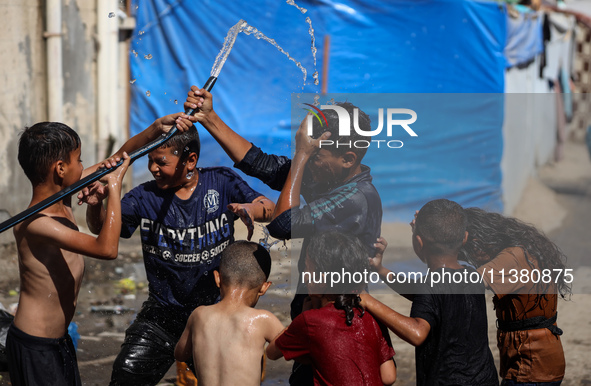 Displaced Palestinian children are playing with water outside their tents during a heat wave in Deir al-Balah in the central Gaza Strip on J...