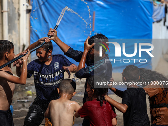 Displaced Palestinian children are playing with water outside their tents during a heat wave in Deir al-Balah in the central Gaza Strip on J...