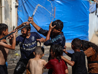 Displaced Palestinian children are playing with water outside their tents during a heat wave in Deir al-Balah in the central Gaza Strip on J...