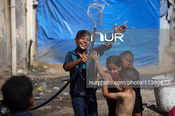 A displaced Palestinian boy is spraying children with water from a pipe outside their tents during a heat wave in Deir al-Balah in the centr...