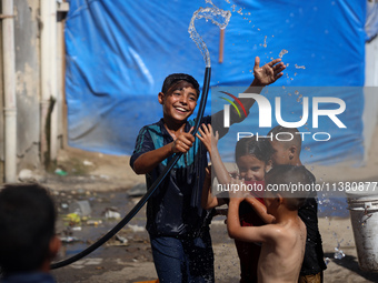 A displaced Palestinian boy is spraying children with water from a pipe outside their tents during a heat wave in Deir al-Balah in the centr...