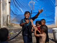 A displaced Palestinian boy is spraying children with water from a pipe outside their tents during a heat wave in Deir al-Balah in the centr...