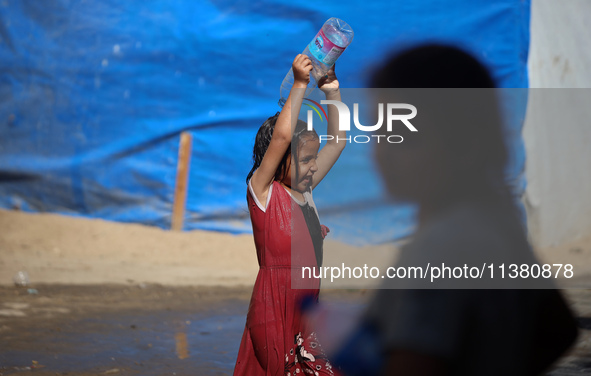 A displaced Palestinian girl is cooling herself with water outside her tent during a heat wave in Deir al-Balah in the central Gaza Strip on...