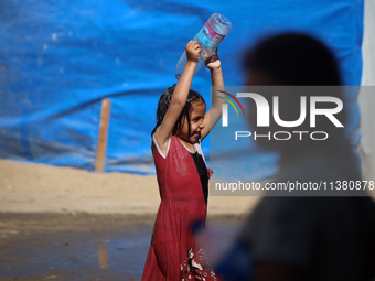 A displaced Palestinian girl is cooling herself with water outside her tent during a heat wave in Deir al-Balah in the central Gaza Strip on...