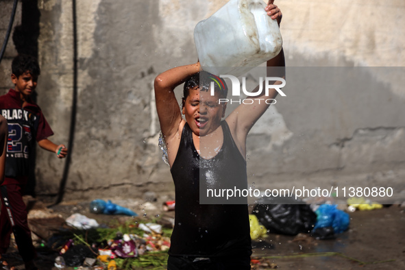 A displaced Palestinian boy is cooling himself with water outside his tent during a heat wave in Deir al-Balah in the central Gaza Strip on...