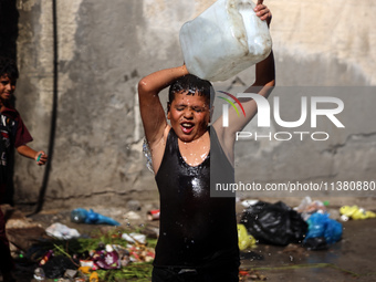 A displaced Palestinian boy is cooling himself with water outside his tent during a heat wave in Deir al-Balah in the central Gaza Strip on...