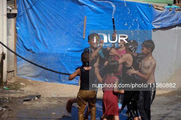 Displaced Palestinian children are playing with water outside their tents during a heat wave in Deir al-Balah in the central Gaza Strip on J...