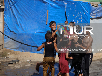 Displaced Palestinian children are playing with water outside their tents during a heat wave in Deir al-Balah in the central Gaza Strip on J...