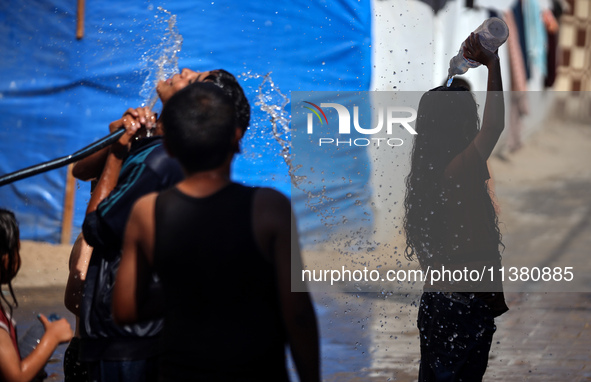 Displaced Palestinian children are playing with water outside their tents during a heat wave in Deir al-Balah in the central Gaza Strip on J...