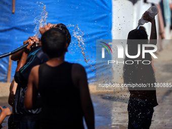 Displaced Palestinian children are playing with water outside their tents during a heat wave in Deir al-Balah in the central Gaza Strip on J...