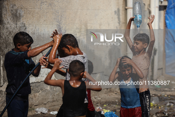 Displaced Palestinian children are playing with water outside their tents during a heat wave in Deir al-Balah in the central Gaza Strip on J...