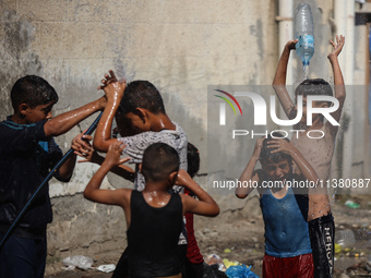 Displaced Palestinian children are playing with water outside their tents during a heat wave in Deir al-Balah in the central Gaza Strip on J...