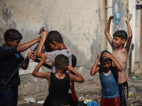 Displaced Palestinian children are playing with water outside their tents during a heat wave in Deir al-Balah in the central Gaza Strip on J...