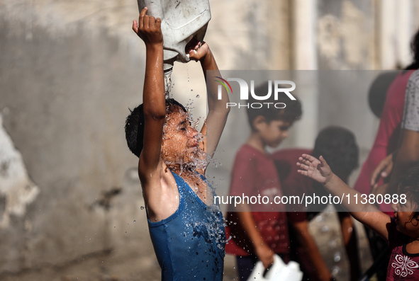 A displaced Palestinian boy is cooling himself with water outside his tent during a heat wave in Deir al-Balah in the central Gaza Strip on...