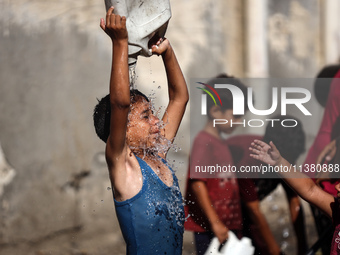 A displaced Palestinian boy is cooling himself with water outside his tent during a heat wave in Deir al-Balah in the central Gaza Strip on...