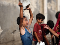 A displaced Palestinian boy is cooling himself with water outside his tent during a heat wave in Deir al-Balah in the central Gaza Strip on...