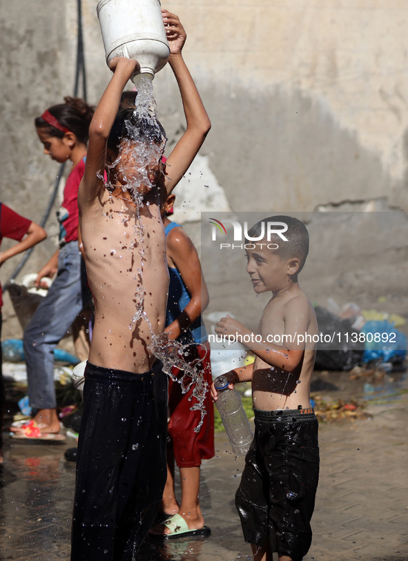 A displaced Palestinian boy is cooling himself with water outside his tent during a heat wave in Deir al-Balah in the central Gaza Strip on...