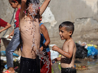 A displaced Palestinian boy is cooling himself with water outside his tent during a heat wave in Deir al-Balah in the central Gaza Strip on...