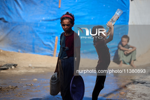 A displaced Palestinian girl is cooling herself with water outside her tent during a heat wave in Deir al-Balah in the central Gaza Strip on...