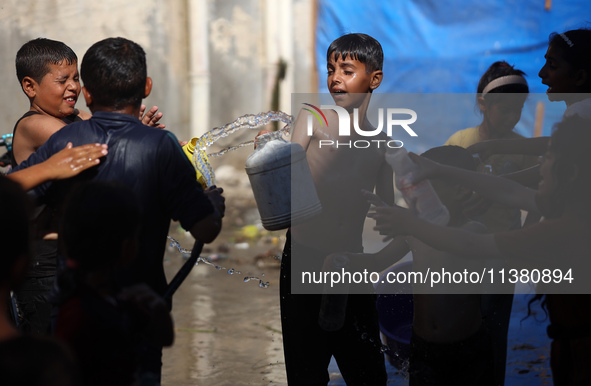 A displaced Palestinian boy is spraying children with water from a pipe outside their tents during a heat wave in Deir al-Balah in the centr...