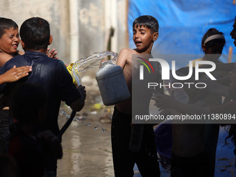 A displaced Palestinian boy is spraying children with water from a pipe outside their tents during a heat wave in Deir al-Balah in the centr...