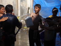 A displaced Palestinian boy is spraying children with water from a pipe outside their tents during a heat wave in Deir al-Balah in the centr...