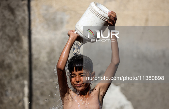 A displaced Palestinian boy is cooling himself with water outside his tent during a heat wave in Deir al-Balah in the central Gaza Strip on...