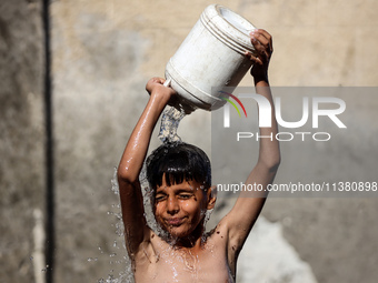 A displaced Palestinian boy is cooling himself with water outside his tent during a heat wave in Deir al-Balah in the central Gaza Strip on...