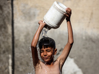 A displaced Palestinian boy is cooling himself with water outside his tent during a heat wave in Deir al-Balah in the central Gaza Strip on...