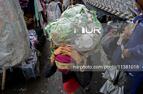 A woman is carrying heavy loads on her head in Darjeeling, India, on July 2, 2024. People are shopping in a vegetable market in Darjeeling,...