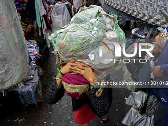 A woman is carrying heavy loads on her head in Darjeeling, India, on July 2, 2024. People are shopping in a vegetable market in Darjeeling,...